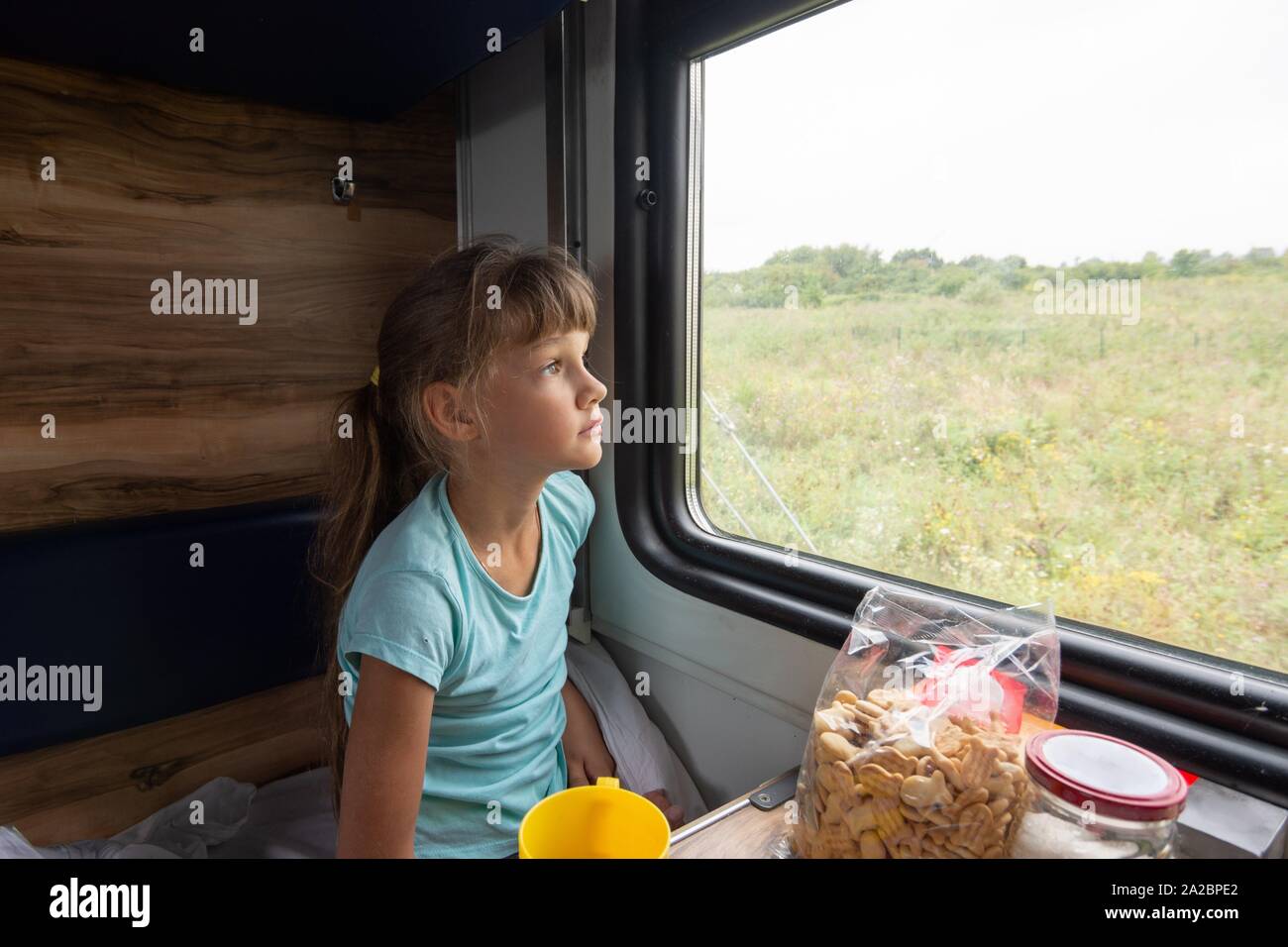 Girl sitting in a reserved seat wagon looks tiredly out the window. Stock Photo
