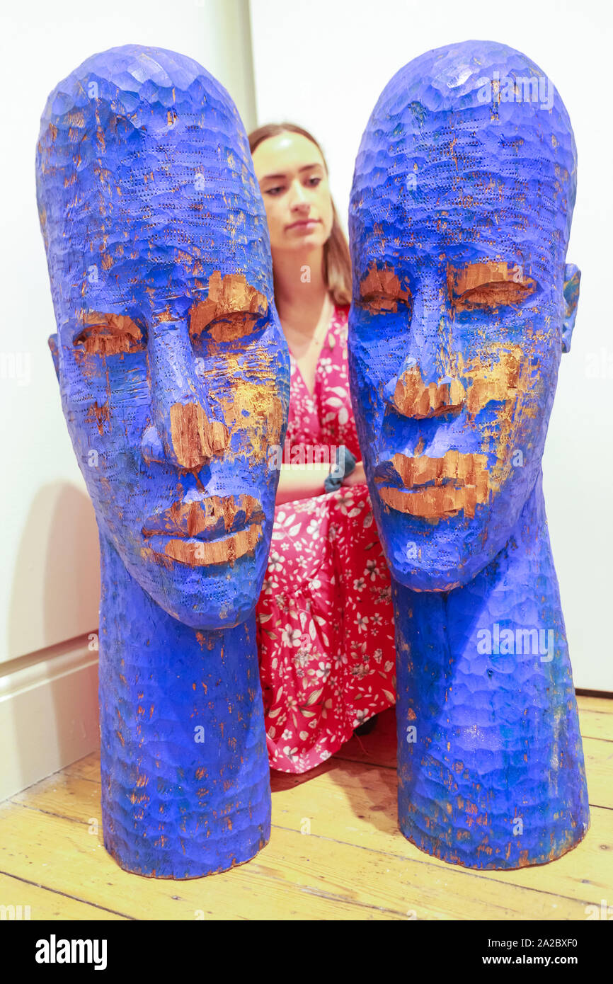 Somerset House, London, UK, 02 Oct 2019. An assistant poses with the wooden sculptures 'Blue Heads' by artist Prince Gyasi, presented by Nil Gallery Paris. Somerset House, in partnership with 1-54, presents the Contemporary African Art Fair, now in its 7th year at Somerset House. The Fair runs from Oct 3-6 and brings together 45 leading galleries with over 140 artists. Credit: Imageplotter/Alamy Live News Stock Photo