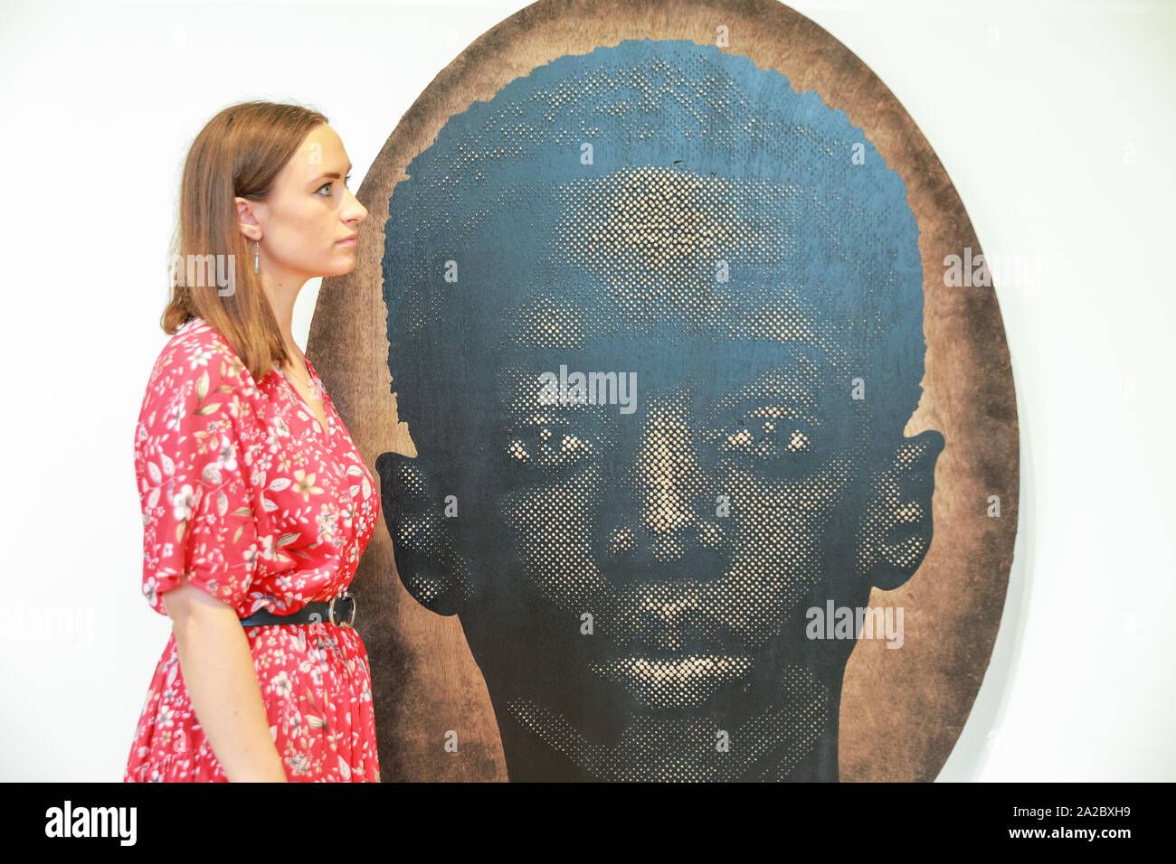 Somerset House, London, UK, 02 Oct 2019. An assistant poses with Alexis Peskine's work 'Dexu Adüna', (2019)',which deals with racian and ethnic identity. Somerset House, in partnership with 1-54, presents the Contemporary African Art Fair, now in its 7th year at Somerset House. The Fair runs from Oct 3-6 and brings together 45 leading galleries with over 140 artists. Credit: Imageplotter/Alamy Live News Stock Photo