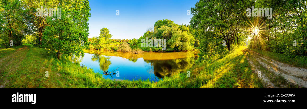 Landschaft im Sommer mit Fluss, Sonne, Weg und Wald Stock Photo