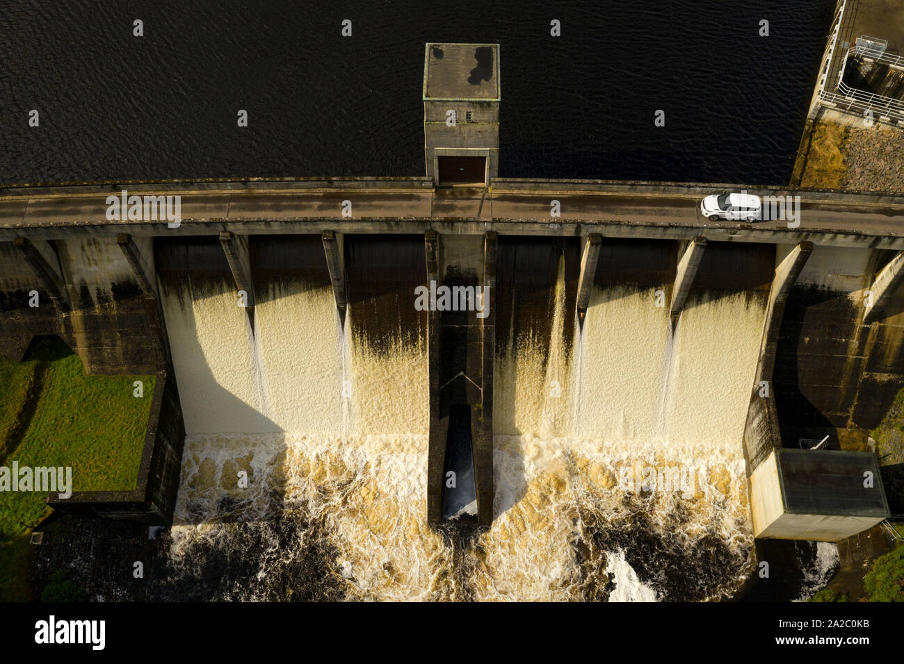 Water flowing over the Meig Hydro Electric Dam in Highland Scotland, with a Land Rover Evoque car driving over the public Road over the dam. Stock Photo