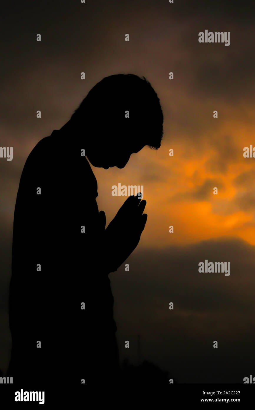 A 12 year old silhouette boy praying at sunset. Stock Photo