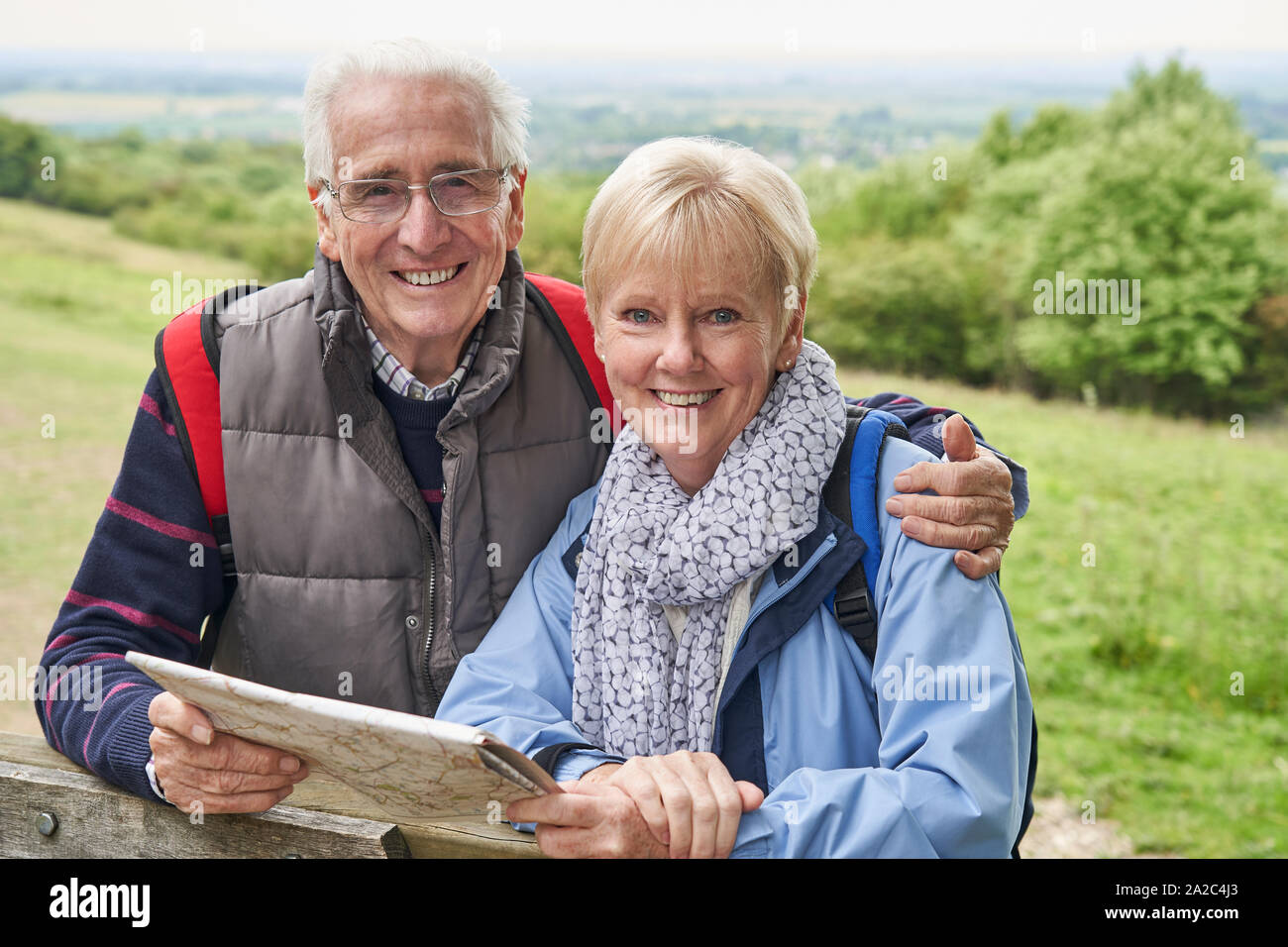 Portrait Of Retired Couple On Walking Holiday Resting On Gate With Map Stock Photo