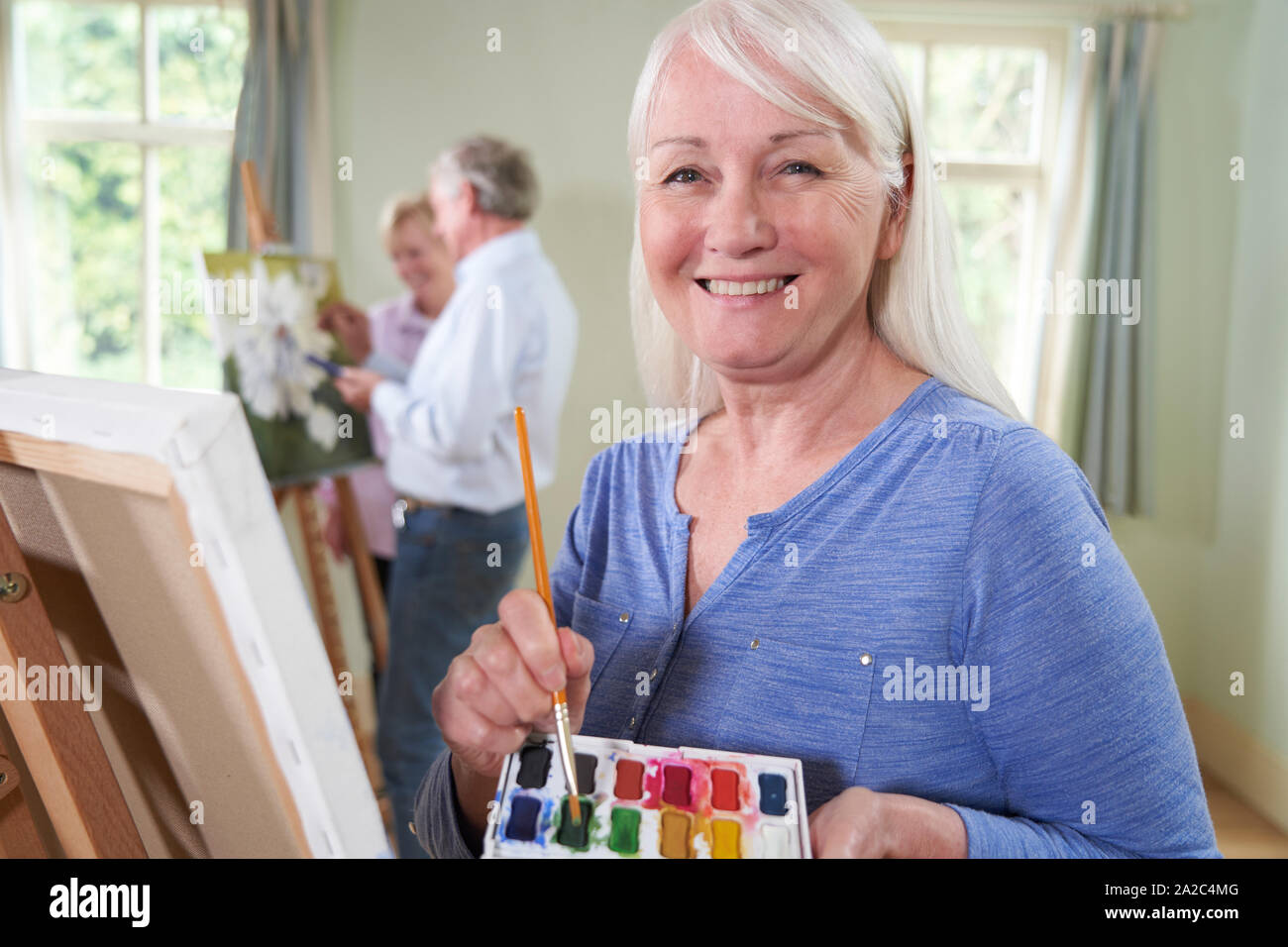 Portrait Of Senior Woman Attending Painting Class With Teacher          In Background Stock Photo