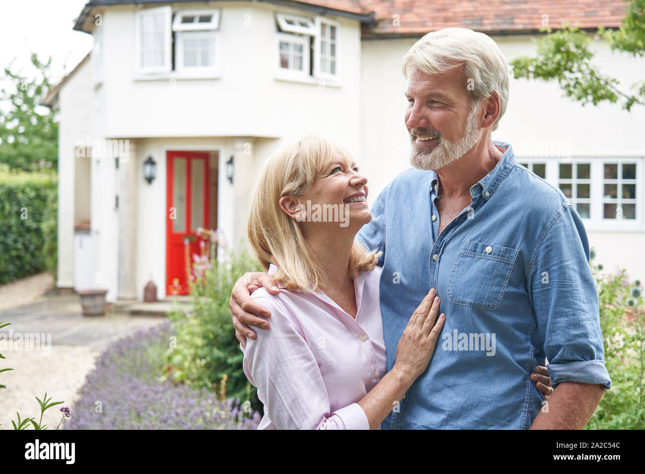 Mature Couple Standing In Garden In Front Of Dream Home In Countryside Stock Photo