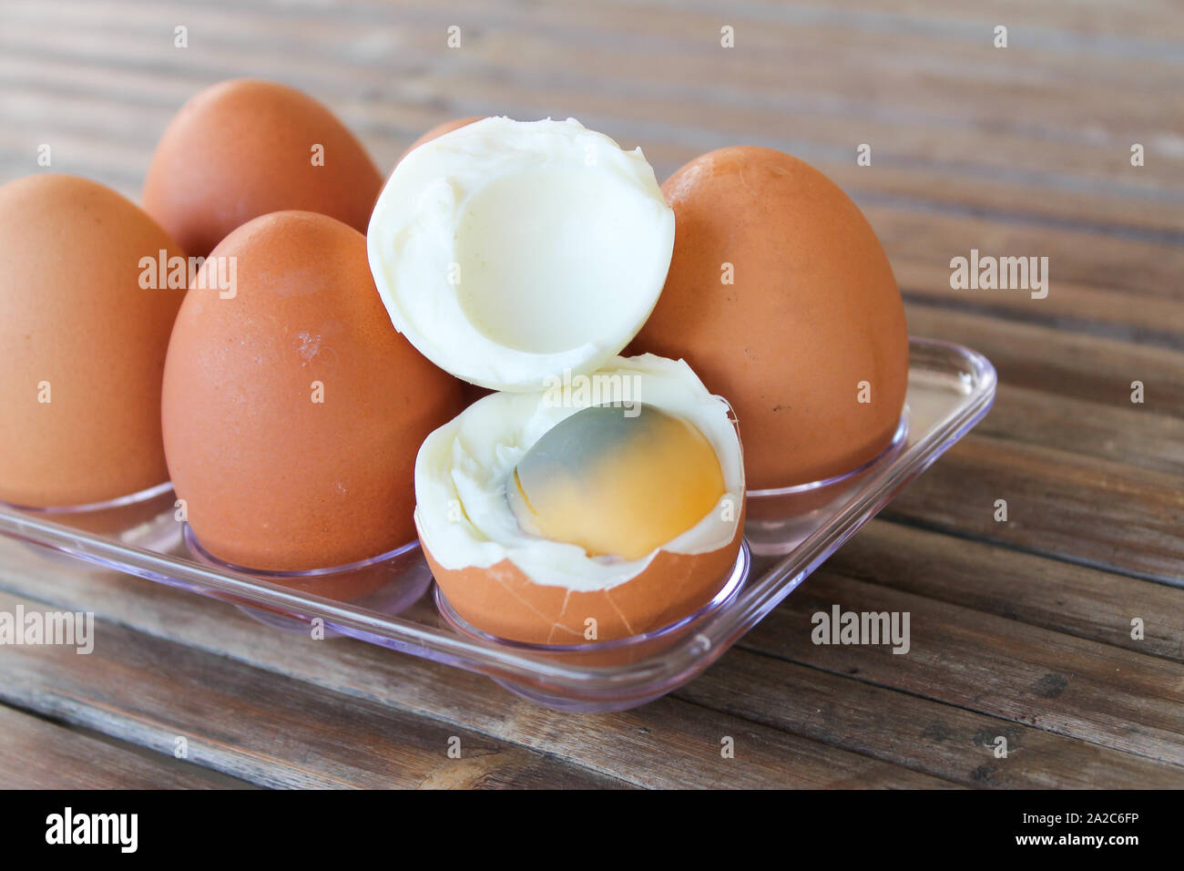 close up Six brown eggs in plastic box on bamboo table with one broken boiled egg, top view. Stock Photo