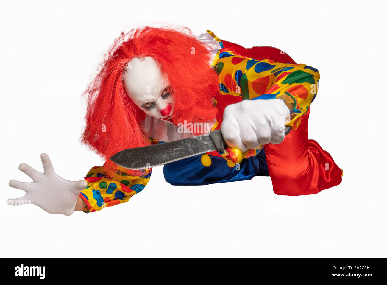 bad clown lies on the ground and holds a knife in the camera Stock Photo
