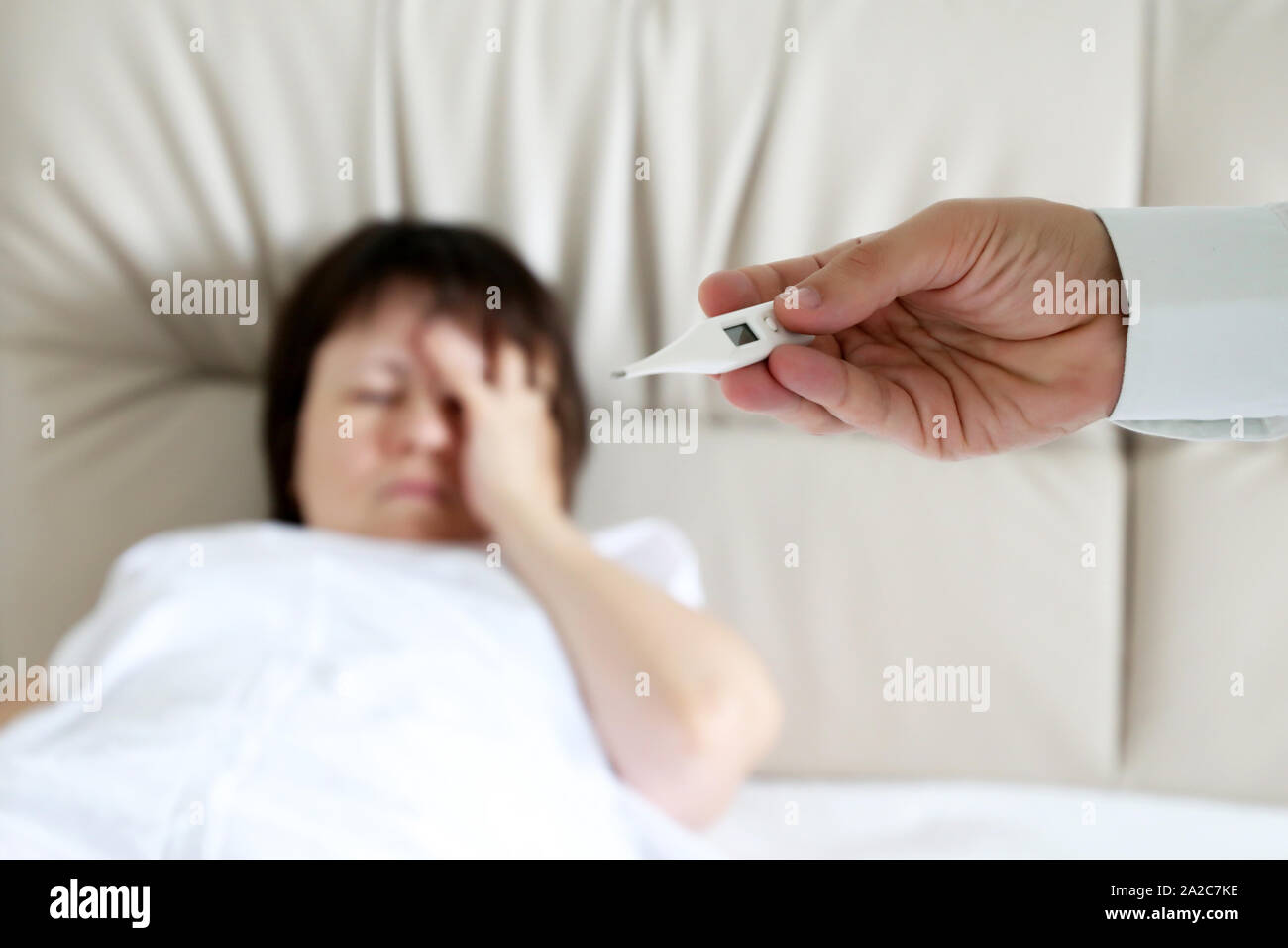 Fever and illness, sick woman lying in a bed, digital thermometer in male hand close up. Doctor measuring body temperature of patient, cold anв flu Stock Photo