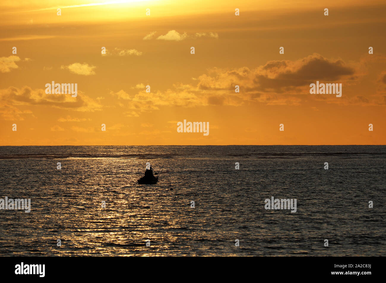 Sunset over the sea, black silhouette of a boat with people on horizon. Dramatic orange sky with clouds, concept of ship in distress, lost in ocean Stock Photo