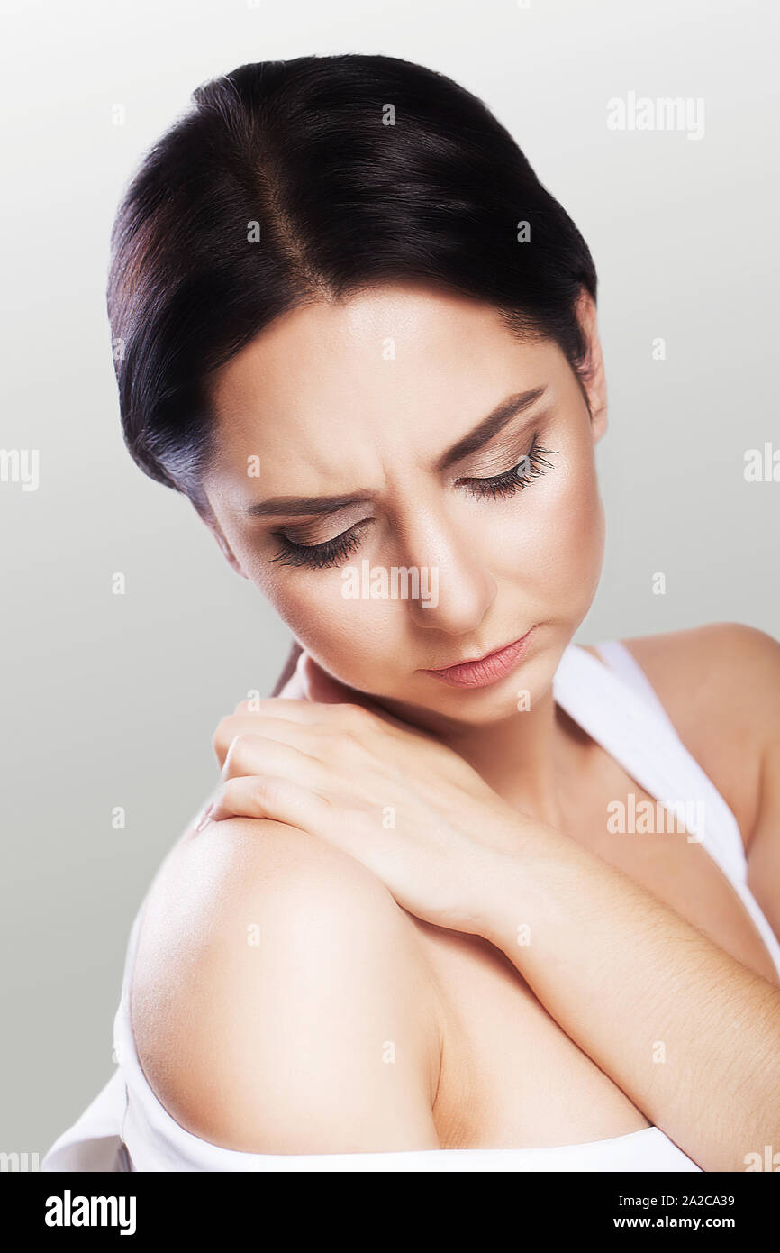 Muscle pain. Shoulders A young woman holds her hand over her shoulders. Cold. Overfatigue. The concept of health. On a gray background. Stock Photo