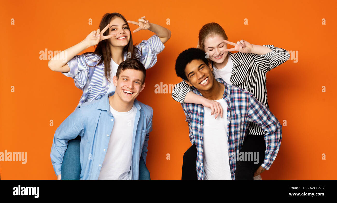 Excited teen guys giving piggyback ride to girls Stock Photo
