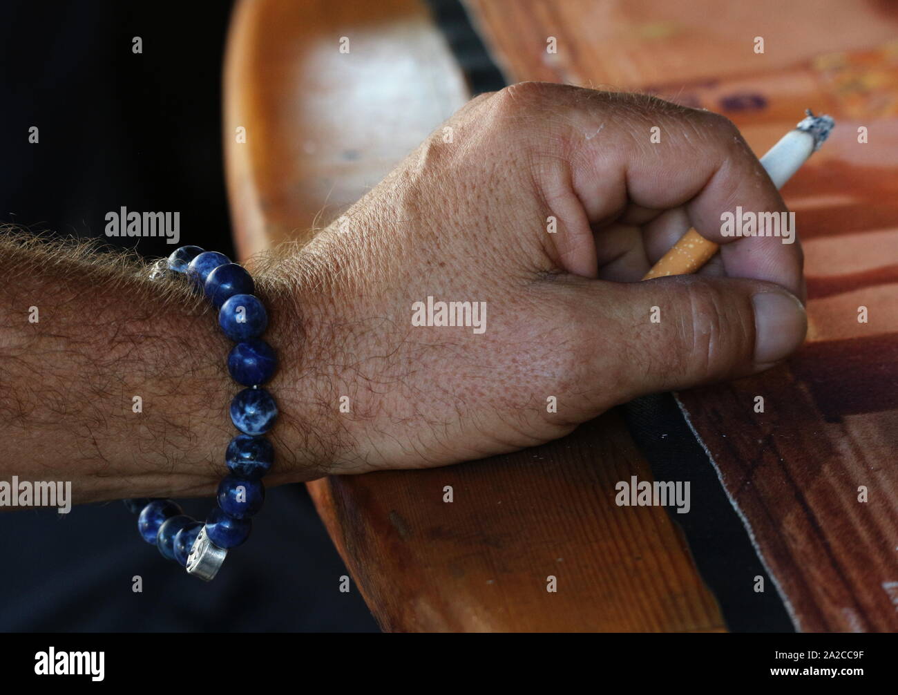 Close up of man's hand holding lit cigarette on a wood bar Stock Photo