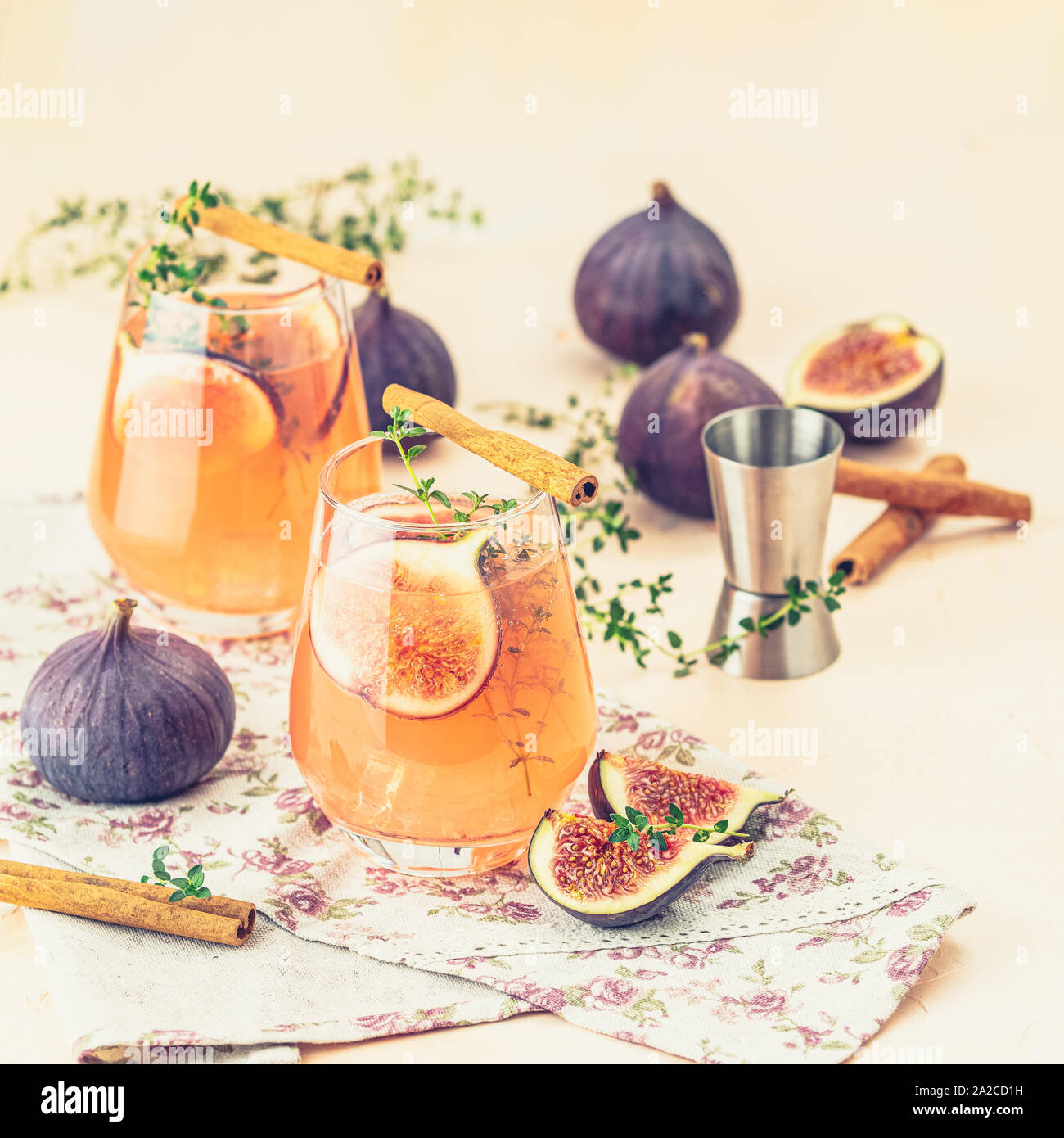 Pink cocktail with fig, thyme and ice in glass on pink concrete