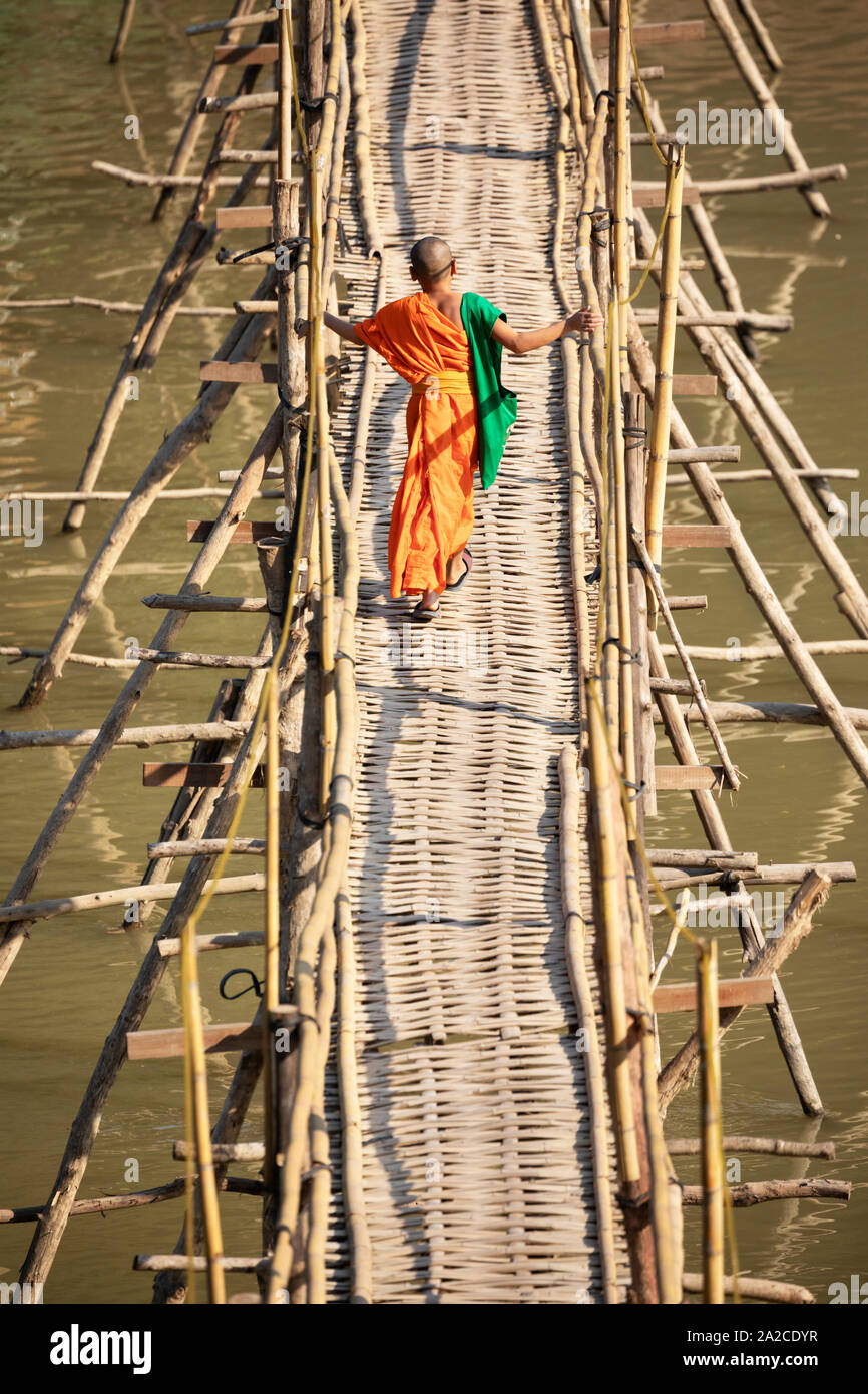 Young Buddhist monk crossing the bamboo footbridge over the Nam Khan River, Luang Prabang, Luang Prabang province, Northern Laos, Laos, Southeast Asia Stock Photo