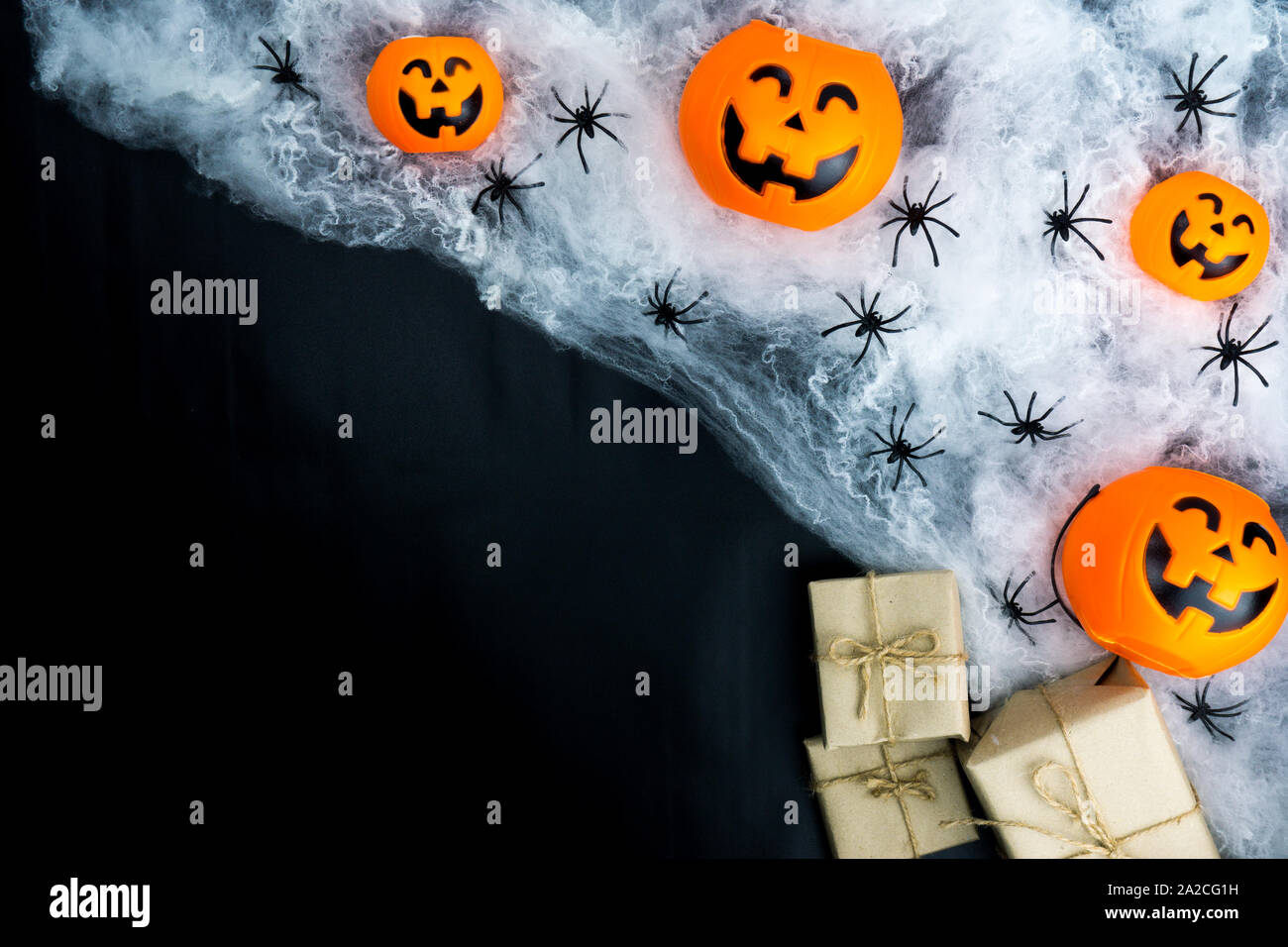 Halloween holiday background with spider, webs, gifts and jack lantern on black background with copy space for text. Flat lay, top view Stock Photo