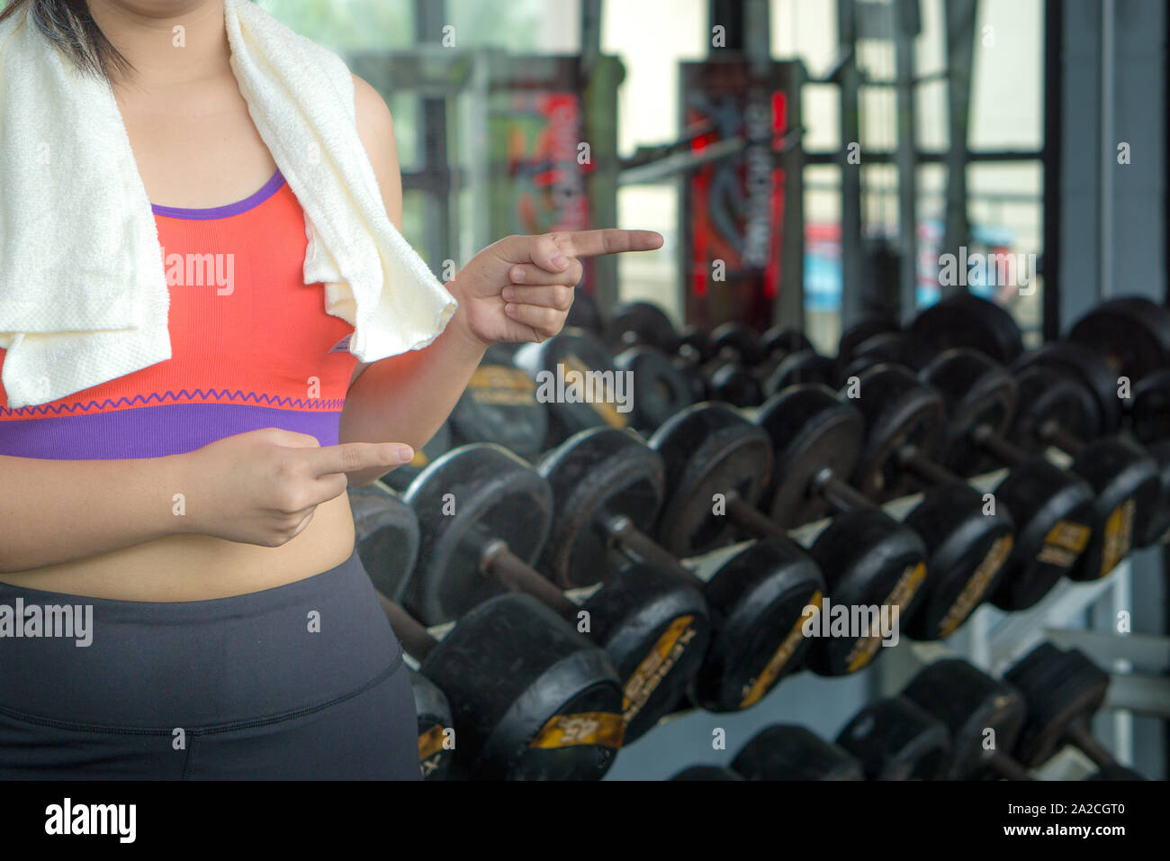 Young woman standing and pointing finger at copy space at fitness gym. Shows free space for your promotional. Stock Photo