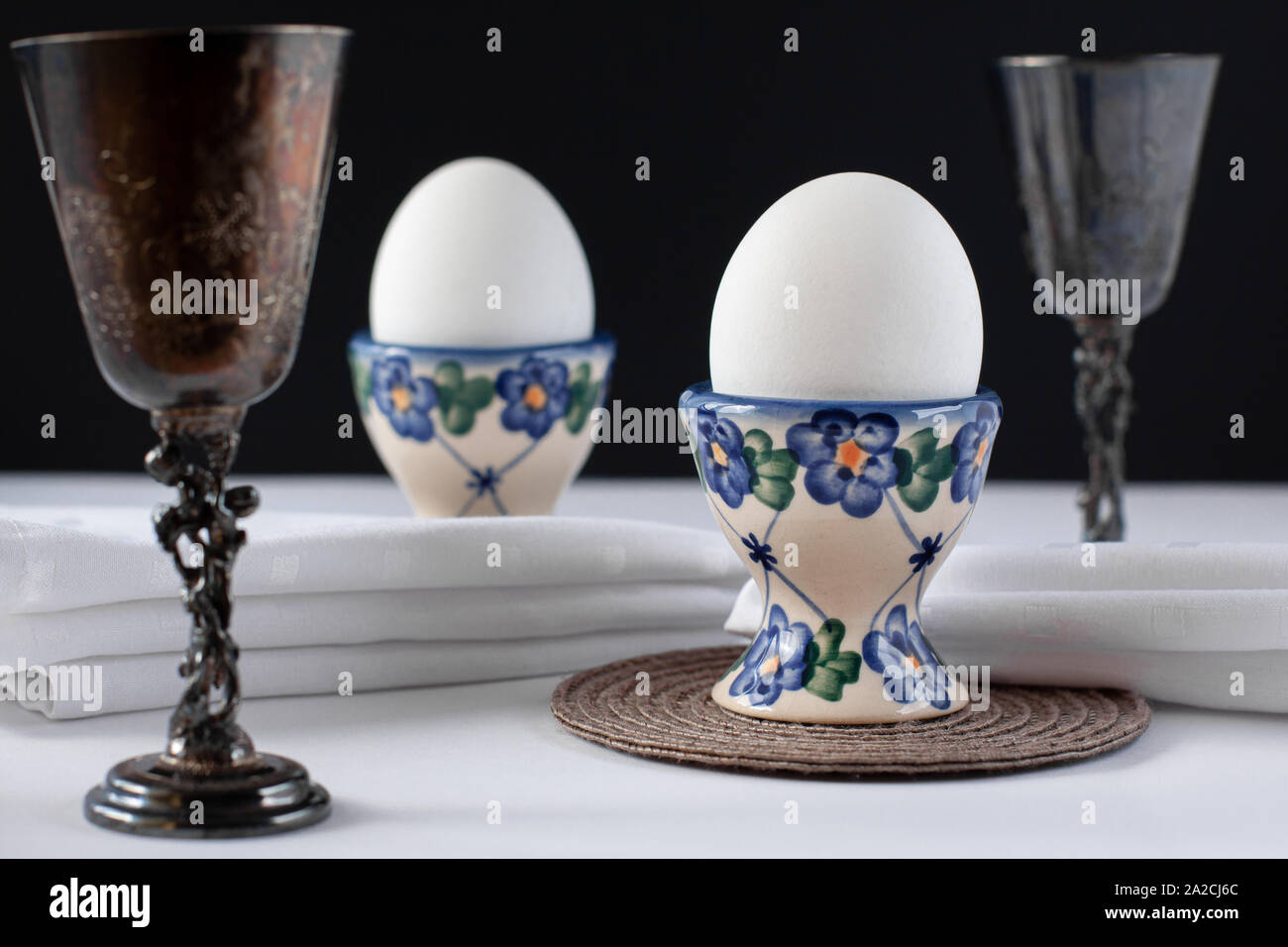 Still life of two white eggs in egg stands with white napkins near it and two sterling silver wine glasses. International world egg day concept Stock Photo