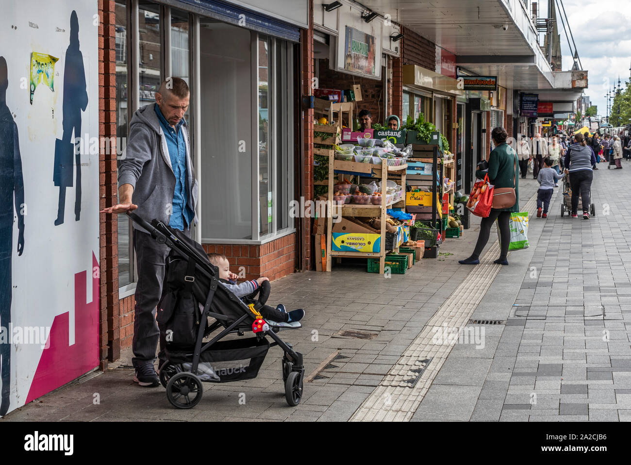 Man waiting with toddler in pushchair,  High Street, West Bromwich, West Midlands, UK. Stock Photo