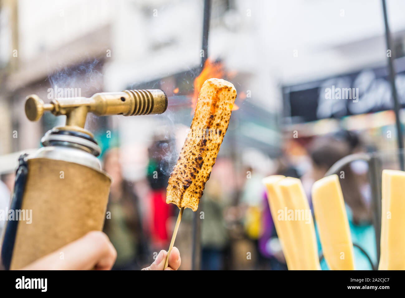 A chef grilling cheese with a kitchen gas torch at a food market Stock