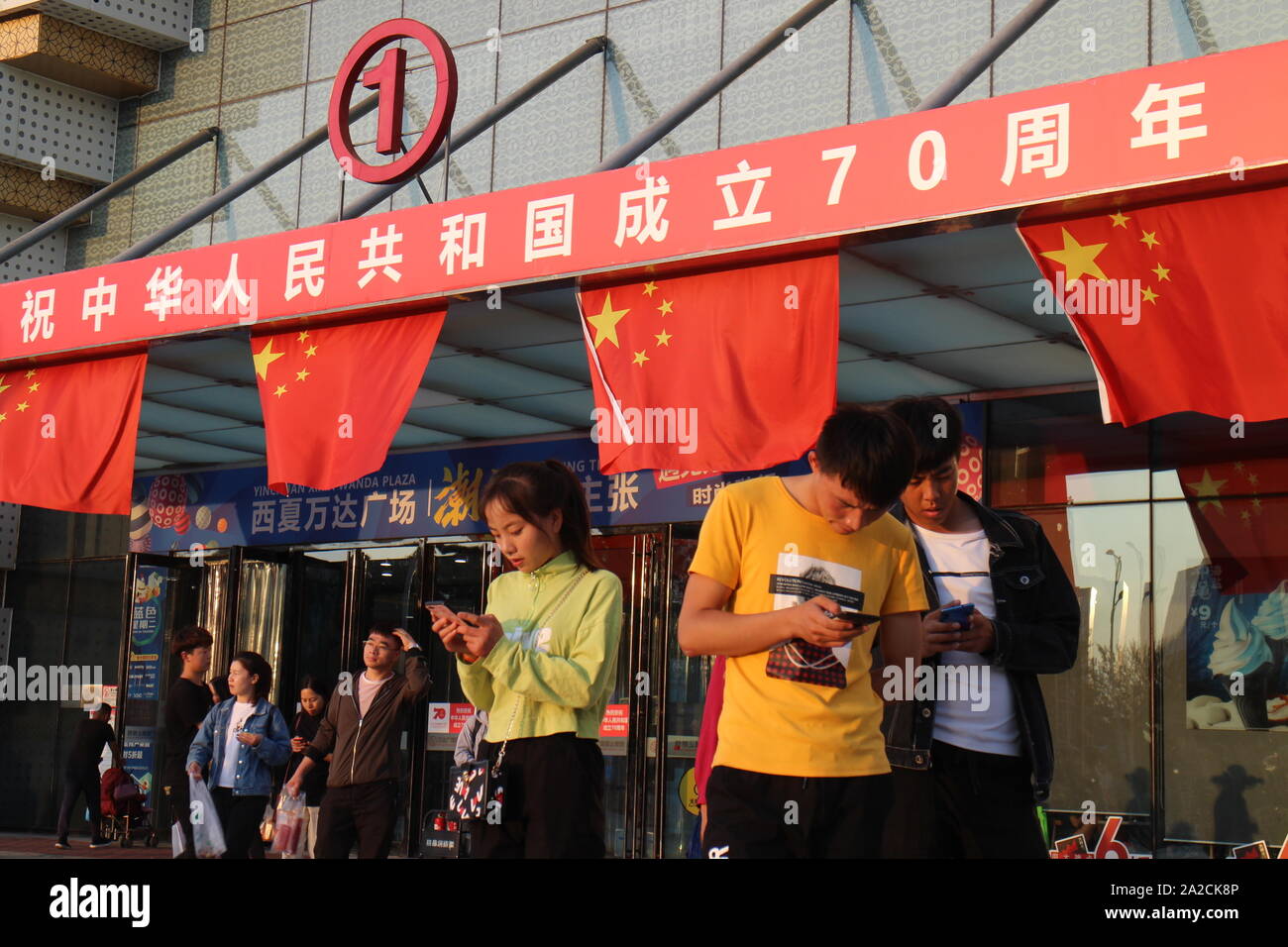 Yinchuan, Ningxia, China. 30th Sep, 2019. A group of teenagers use their  phones in front of Wanda Plaza main entrance decorated with national flags  and the slogan '' Warmest celebrations of the