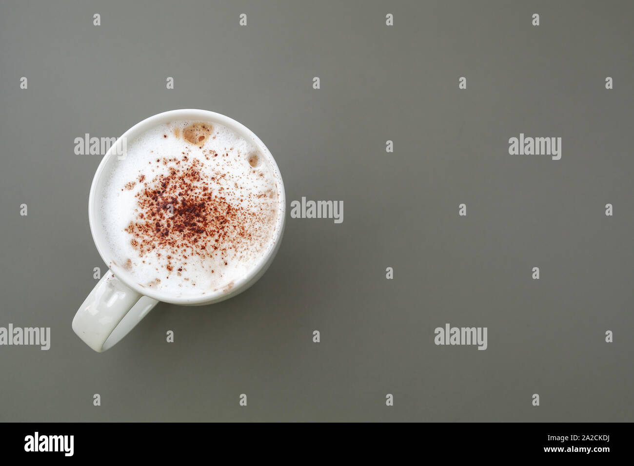 Cappuccino top view. Cup of coffee with milk foam and cinnamon stands on a gray table. Close-up photo with blank copy space area for text on the right Stock Photo