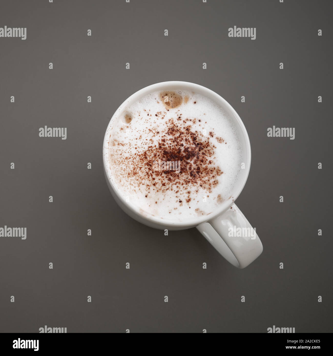 Cappuccino. Cup of coffee with milk foam and cinnamon stands on a gray table, top view. Close-up square photo Stock Photo