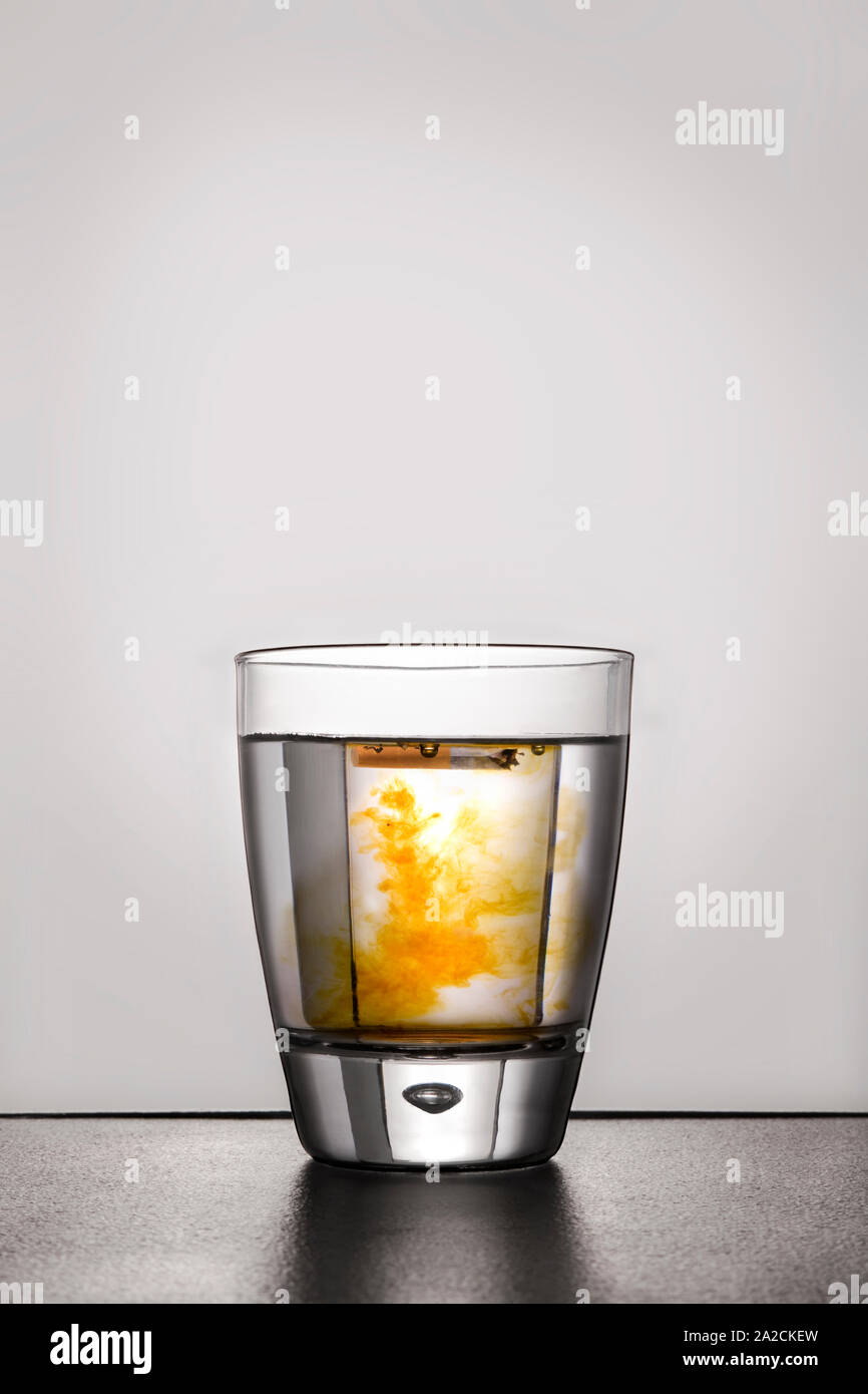 Cigarette in glass of water contaminated with nicotine. Stock Photo