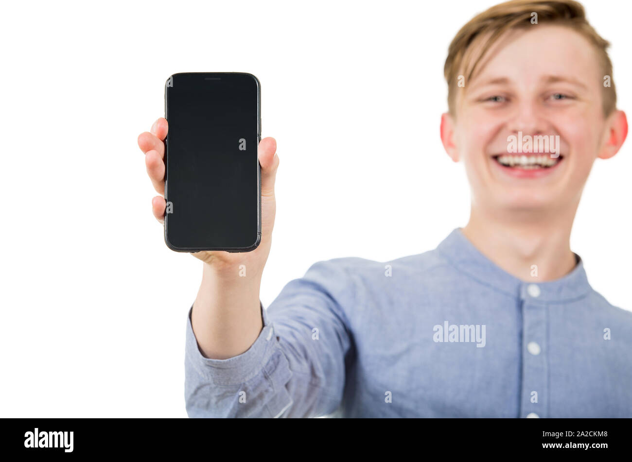 Happy teenager boy showing his smartphone blank screen isolated over white background. Joyful adolescent guy presenting a new device. Stock Photo