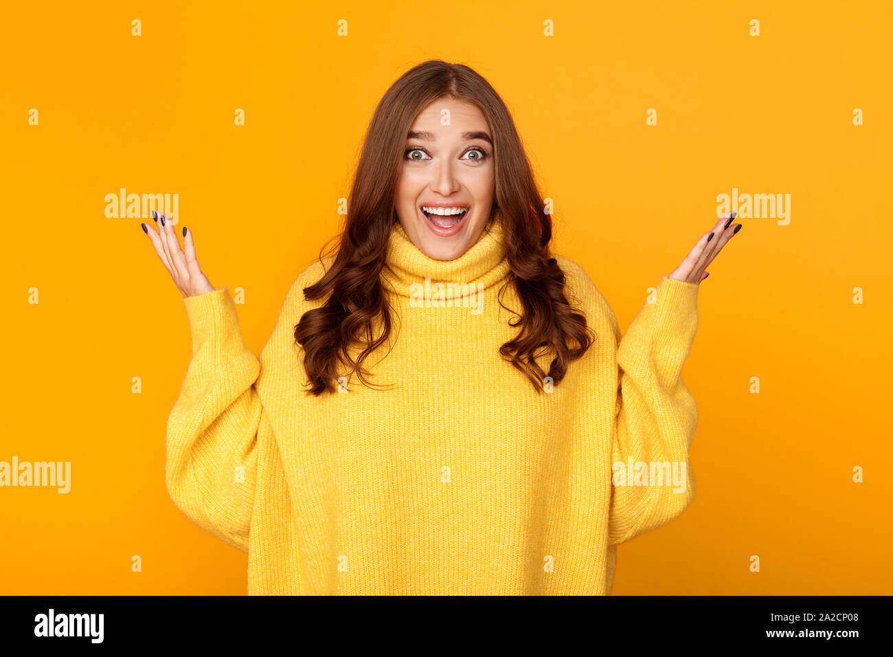 Excited woman raising hands in happiness, yellow background Stock Photo