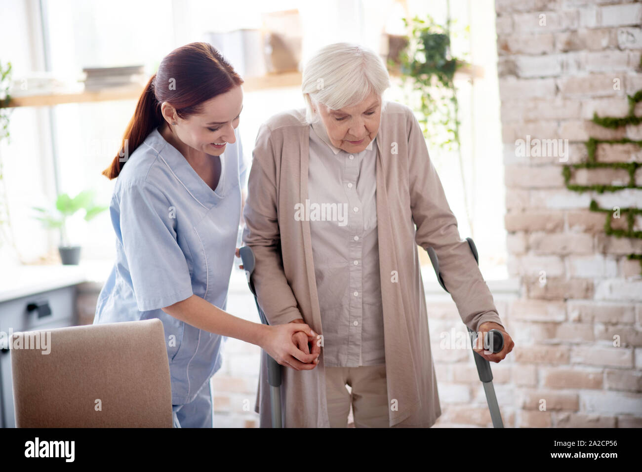 Helpful caregiver assisting woman with crutches Stock Photo