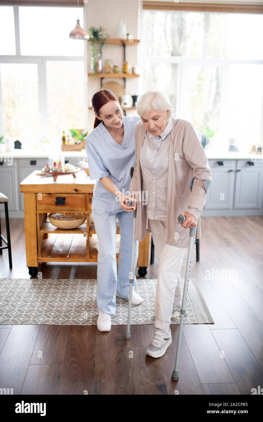 Retired woman making steps with crutches after surgery Stock Photo