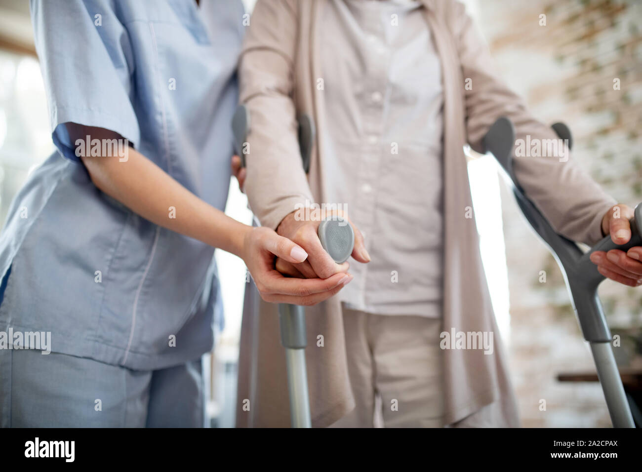 Nurse wearing uniform supporting woman with crutches Stock Photo