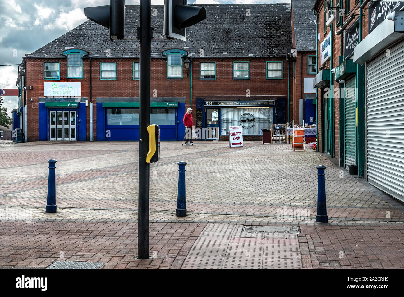 Elderly man walking towards a charity shop in the pedestrian precinct are of Tipton, northwest of Birmingham, West Midlands. The area is surrounded with closed down shops. Stock Photo