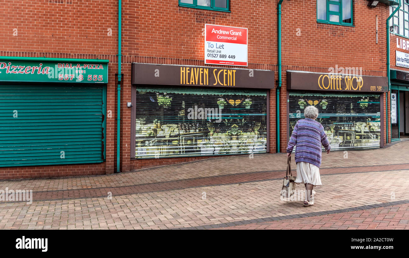 Elderly woman walking past closed down shops in the pedestrian precinct are of Tipton, northwest of Birmingham, West Midlands, UK  With a commerial property let sign in the background. Stock Photo
