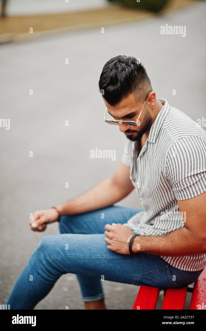 Fashionable tall arab beard man wear on shirt, jeans and sunglasses sitting  on red bench at park Stock Photo - Alamy