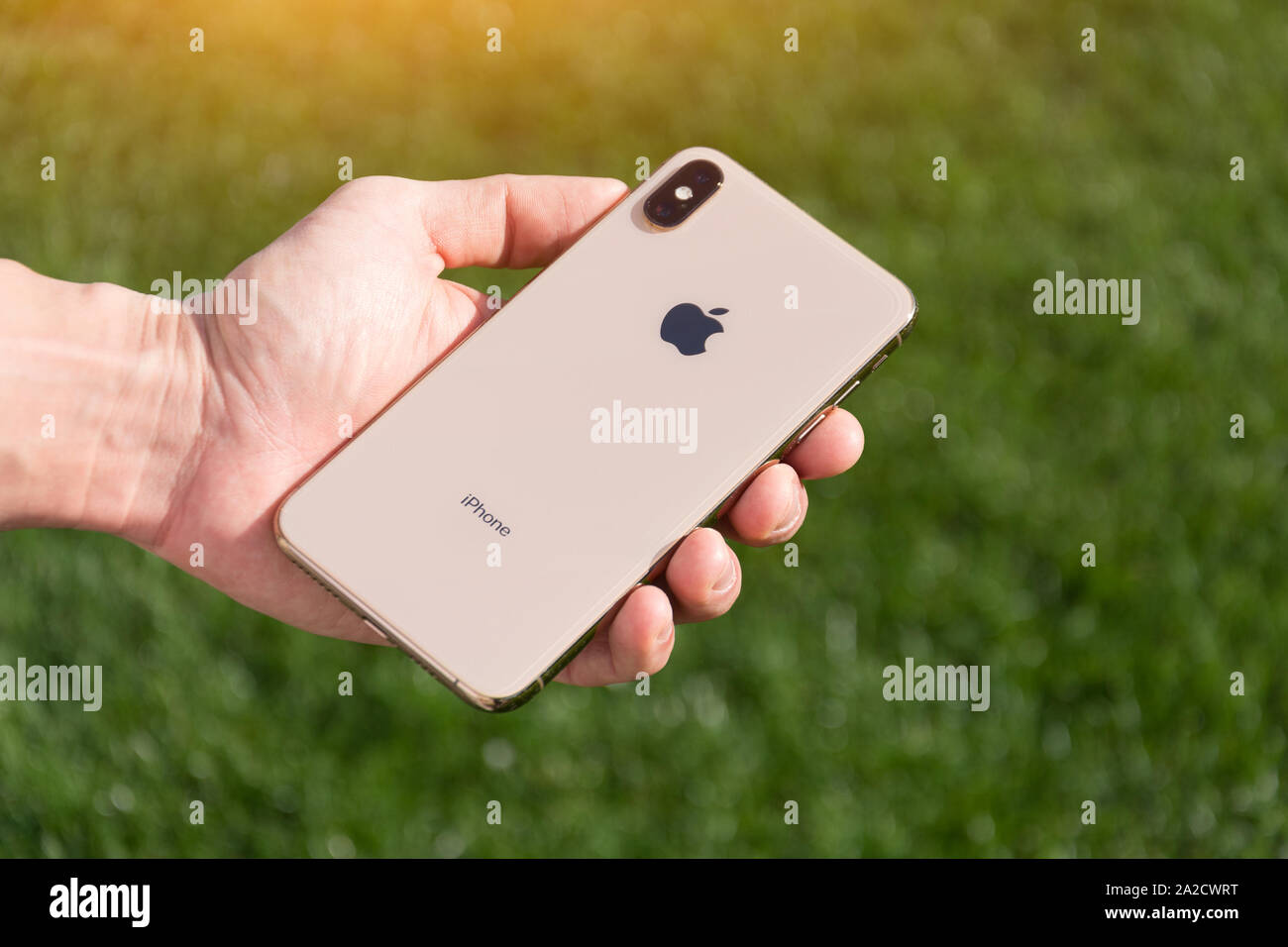 iPhone Xs Max gold smartphone model by Apple Computers close up in male hand on the background of green grass. Italy, Tuscany, Pisa. 26 December 2018 Stock Photo