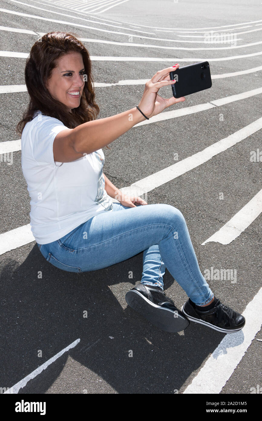 Young woman makes a selfie sitting on the grey floor with white lines. Stock Photo