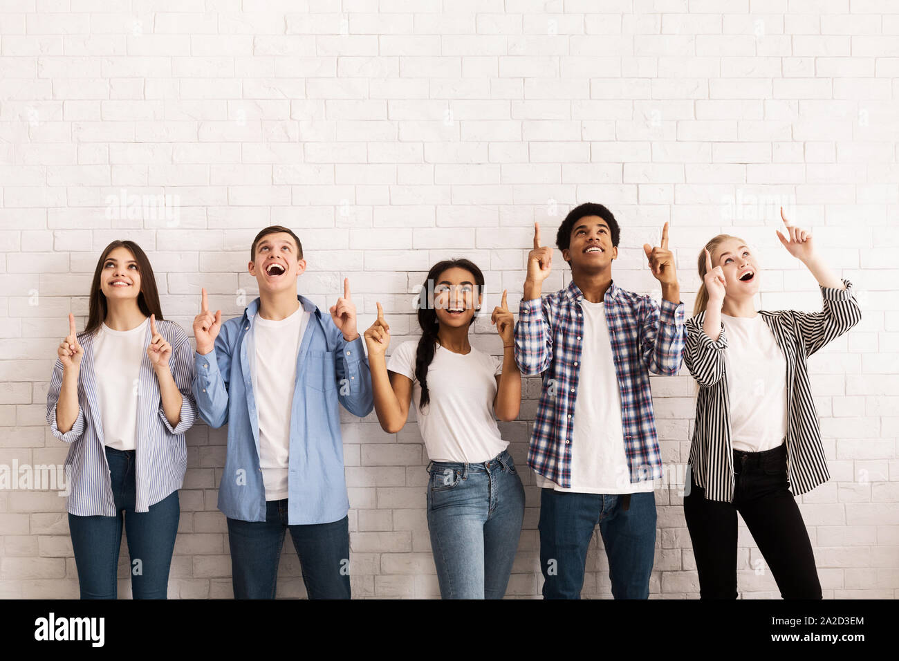 Teen friends pointing up on free space over white wall Stock Photo - Alamy