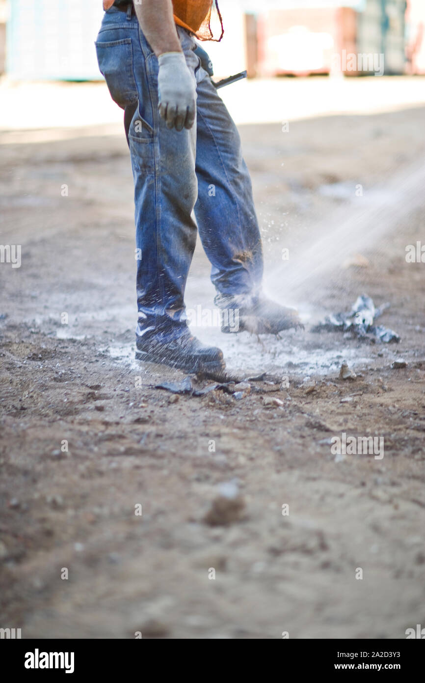 Dirty construction worker cleaning the mud off his work boots with a