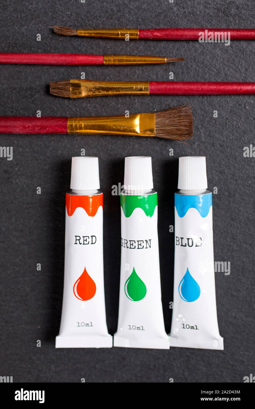 Selection of red green blue paint oils with brushes on a black slate surface Stock Photo