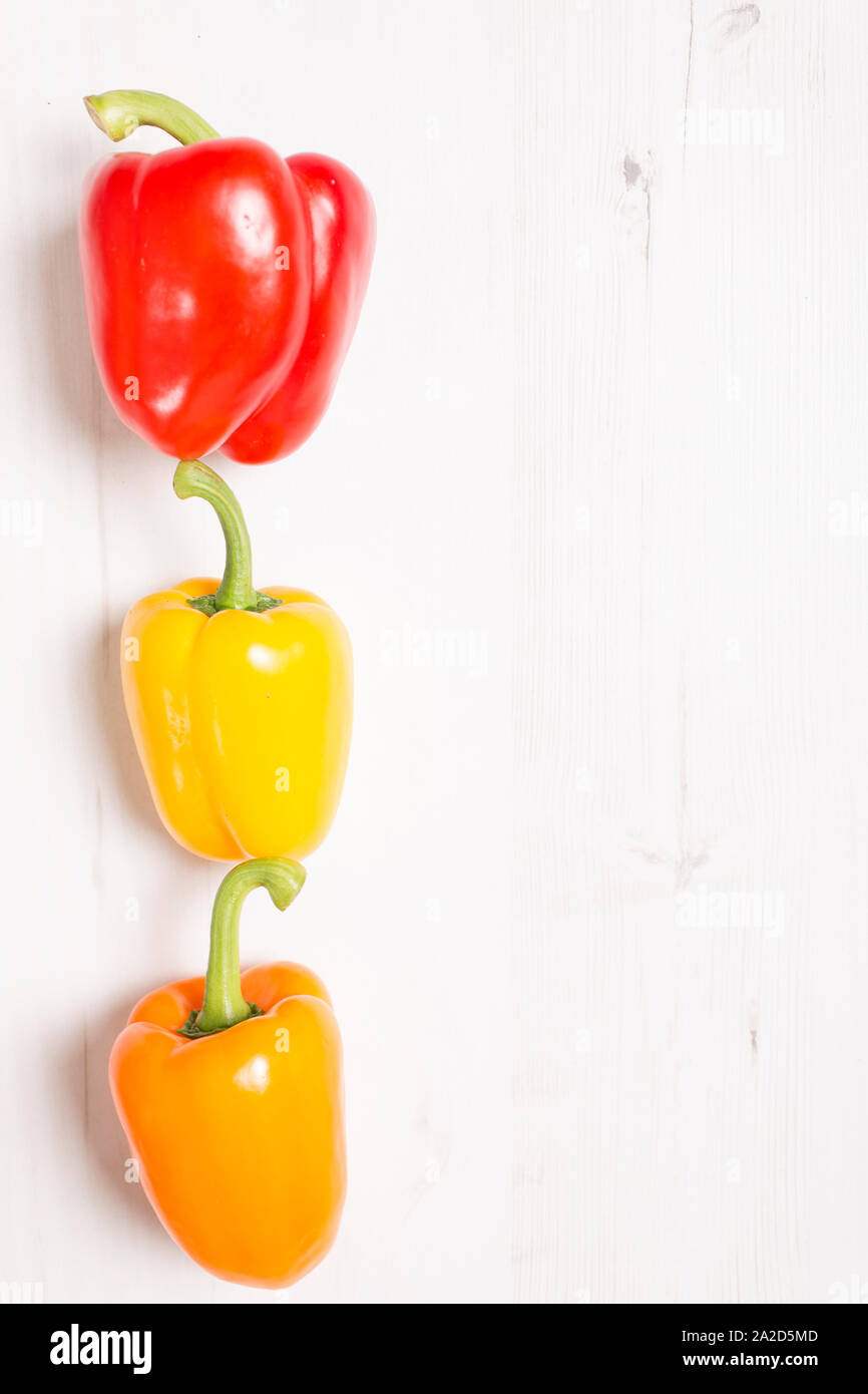 Three fresh red yellow and orange peppers on a light wooden kitchen