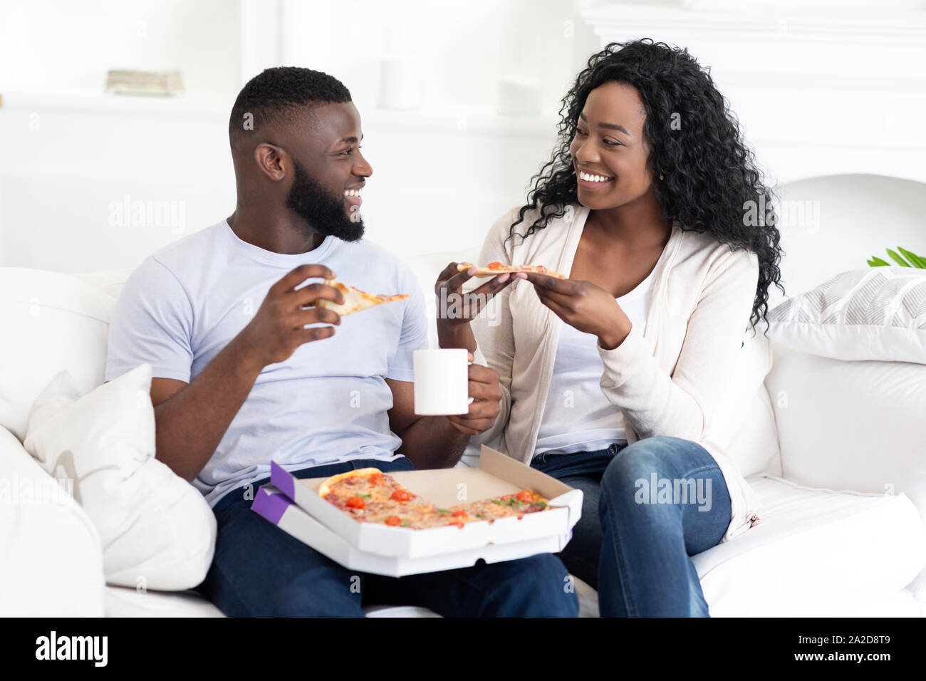 Happy millennial couple eating pizza and drinking coffee at home Stock Photo