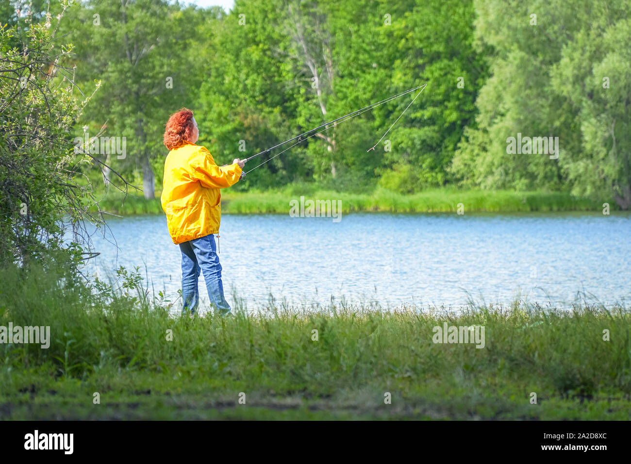 Woman in yellow jacket fishing spinning on the lake Stock Photo - Alamy