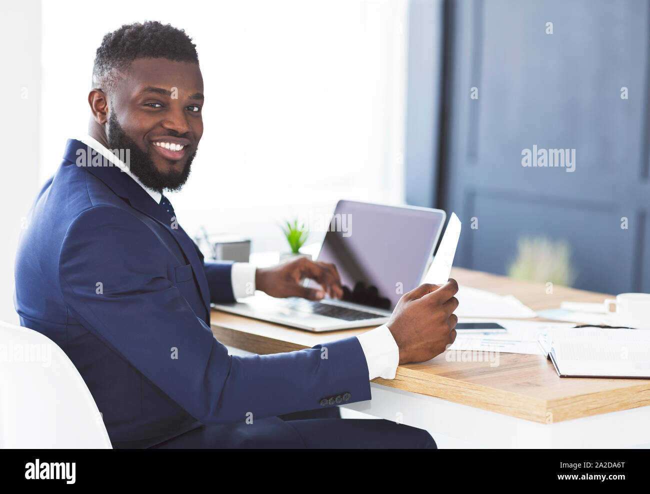 Cheerful black general manager checking reports, sitting in office Stock Photo
