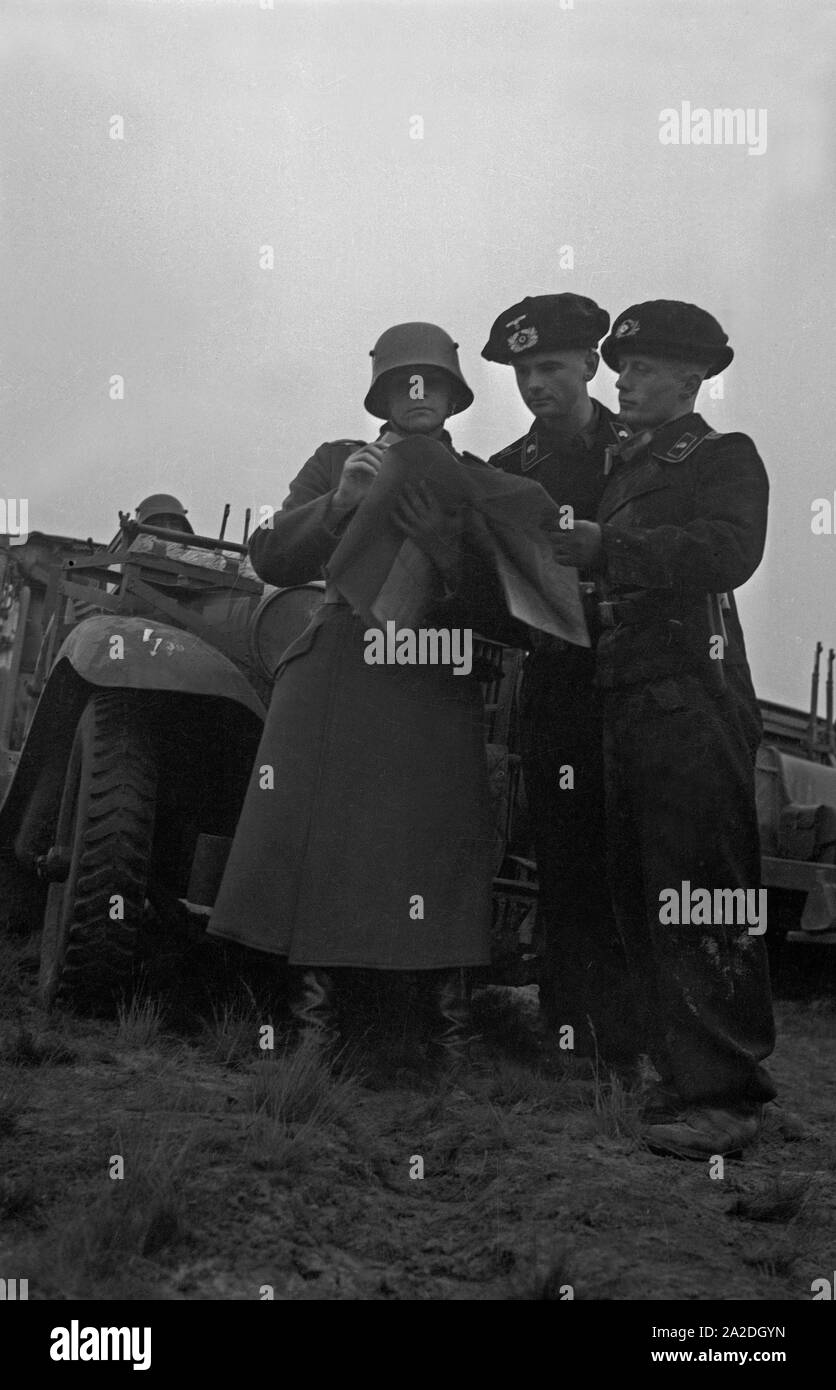 Panzerschützen und ein Meldesoldat vor einem Panzerspähwagen des Typs Sd.Kfz.221 auf einem Truppenübungsplatz, Deutschland 1930er Jahre. Tank crew and soldier in front of an armoured scout car at a military training ground, Germany 1930s. Stock Photo