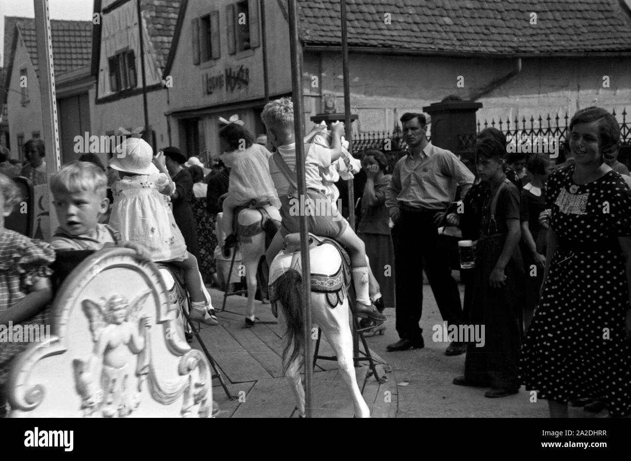 Eltern warten auf ihre Kinder auf dem Karussell beim Rettichfest in Schifferstadt, Deutschland, 1930er Jahre. Parents waiting for their children on a carousel at the annual radish fair at Schifferstadt, Germany 1930s. Stock Photo