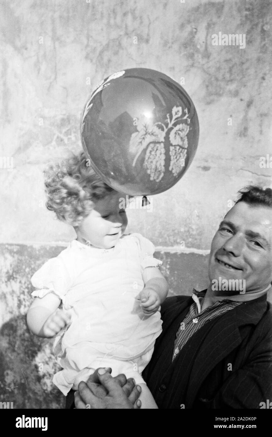 Ein kleines Mädchen mit einem Luftballon auf dem Arm seines Vaters beim Rettichfest in Schifferstadt, Deutschland, 1930er Jahre. A little girl in the arms of her father with a balloon at the annual radish fair at Schifferstadt, Germany 1930s. Stock Photo