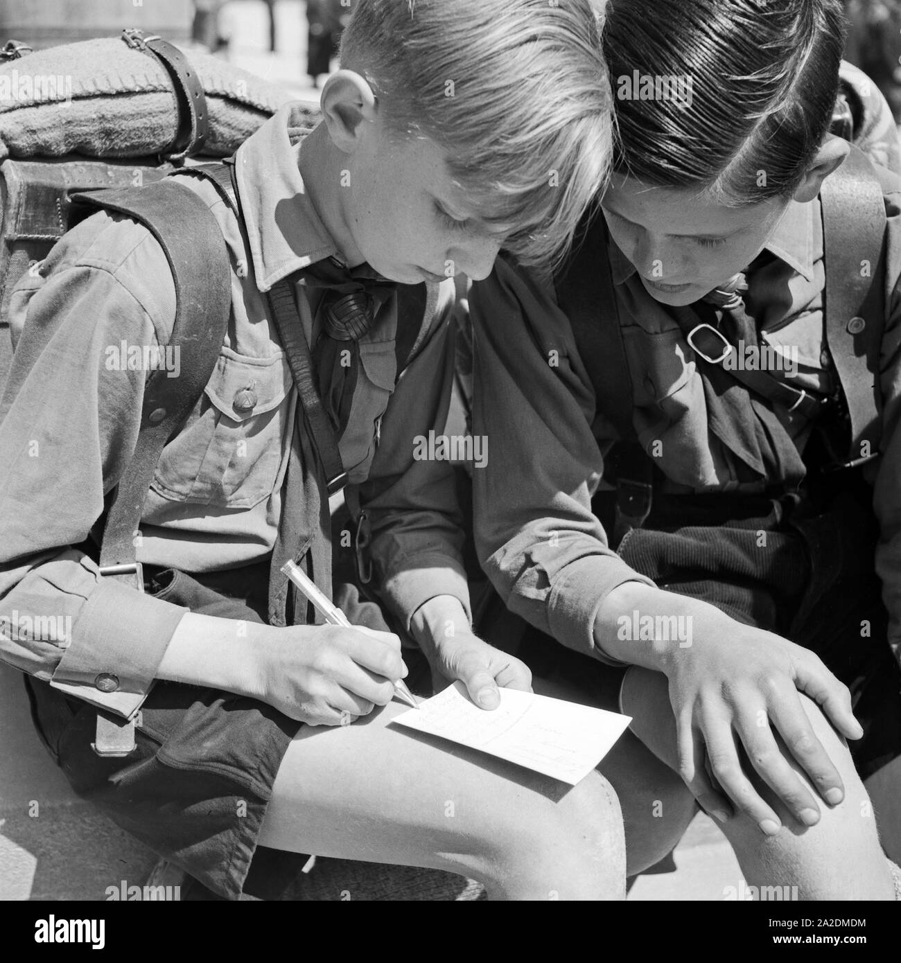 Zwei Hitlerjungen schreiben eine Postkarte von einer Wanderung, Deutschland 1930er Jahre. Two Hitler youths writing a postcard from a wandering trip, Germany 1930s. Stock Photo