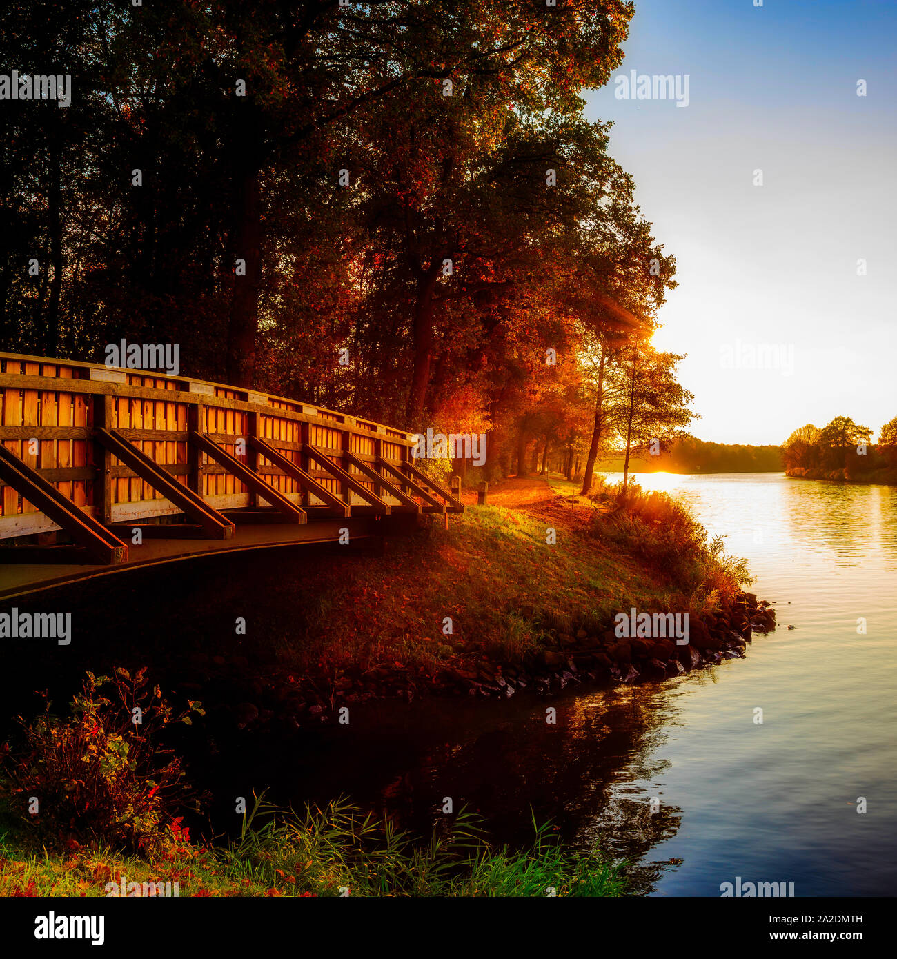 Herbstliche Landschaft an einem Fluss mit Holzbrücke bei Sonnenuntergang Stock Photo
