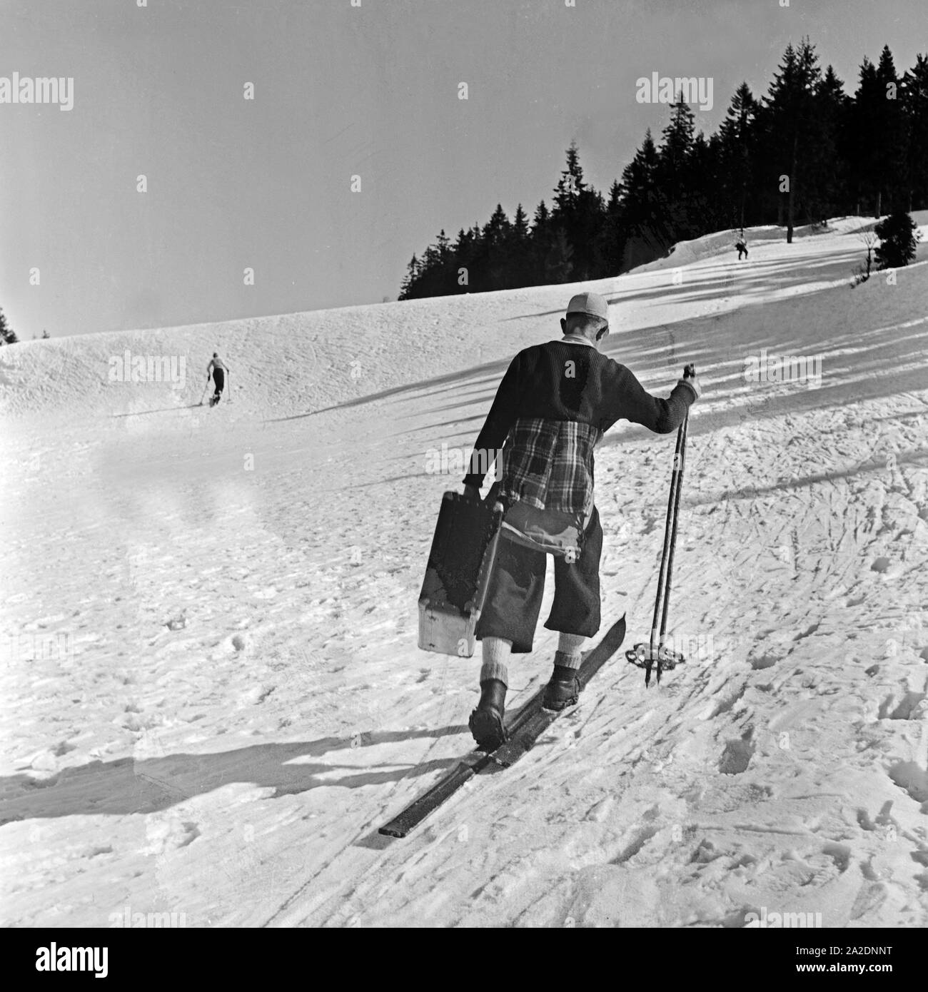 Ein Tourist kommt mit seinem Koffer auf Skiern zum Hotel, Deutschland 1930er Jahre. A tourist skiing with his suitcase to the hotel, Germany 1930s. Stock Photo